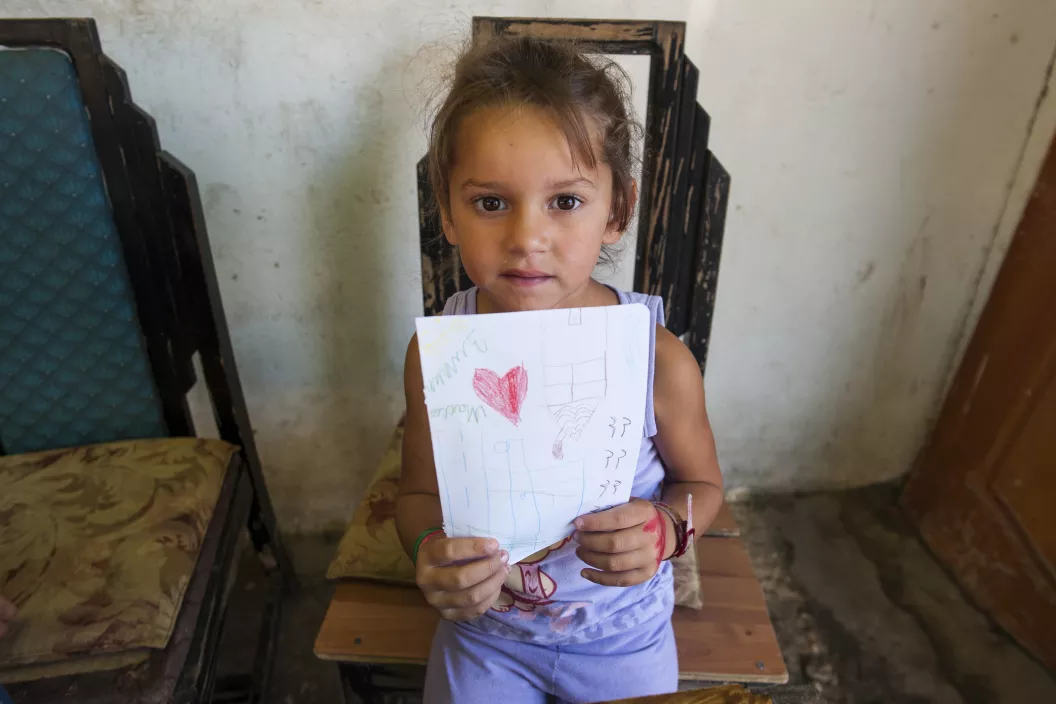 Roma girl holding a paper with her drawing of a red heart